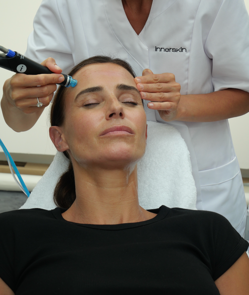 Une femme brune reçoit un soin HydraFacial par une praticienne dans un centre de médecine esthétique.